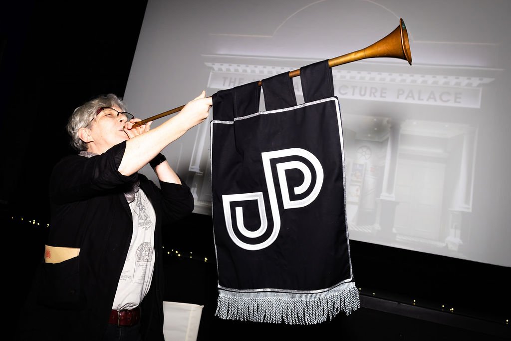 Someone blowing a large trumpet with a UPP banner hanging from it.